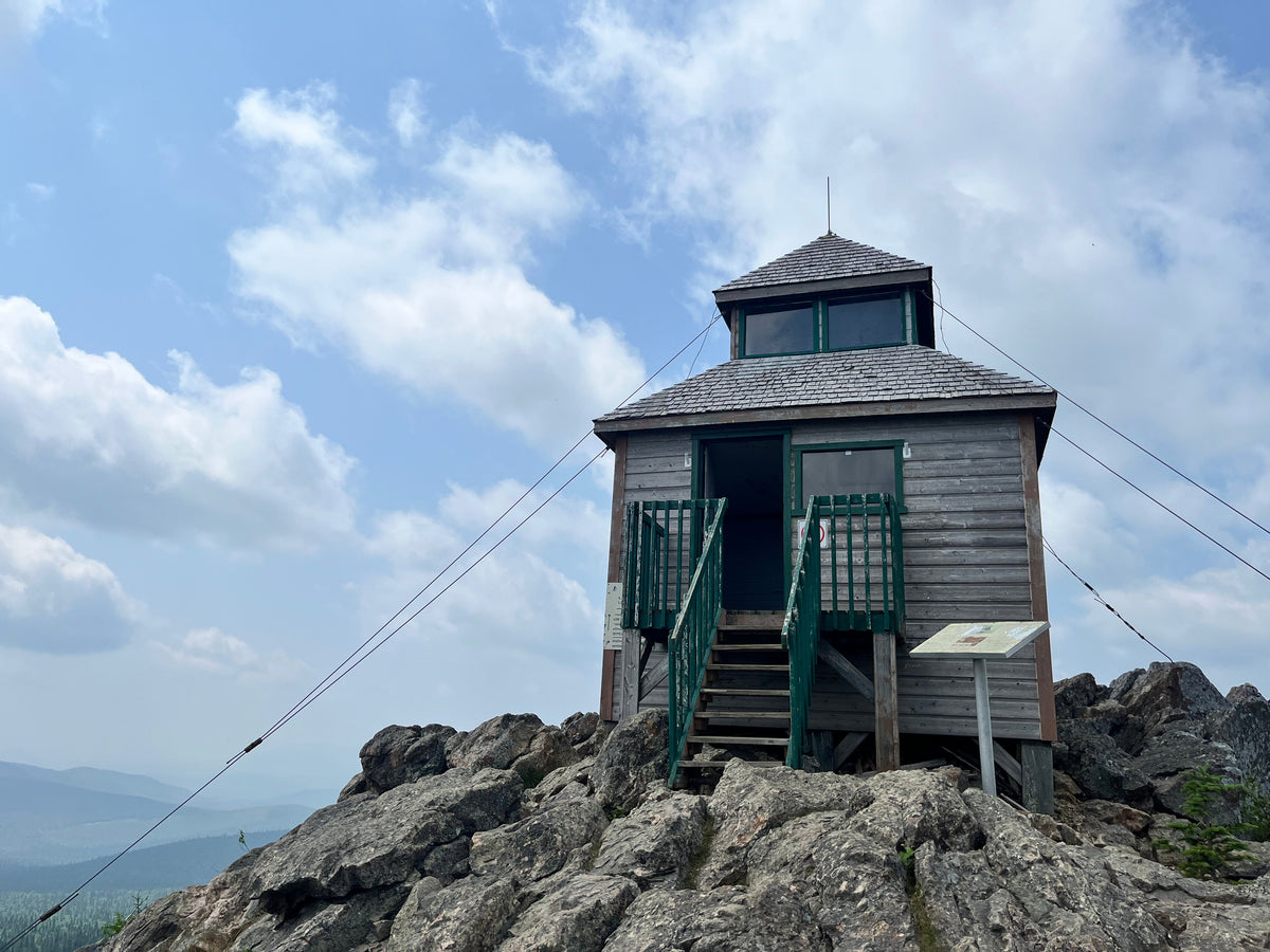 Wooden observation hut on the rocky summit of Mount Carleton beneath a blue, cloud-filled sky.